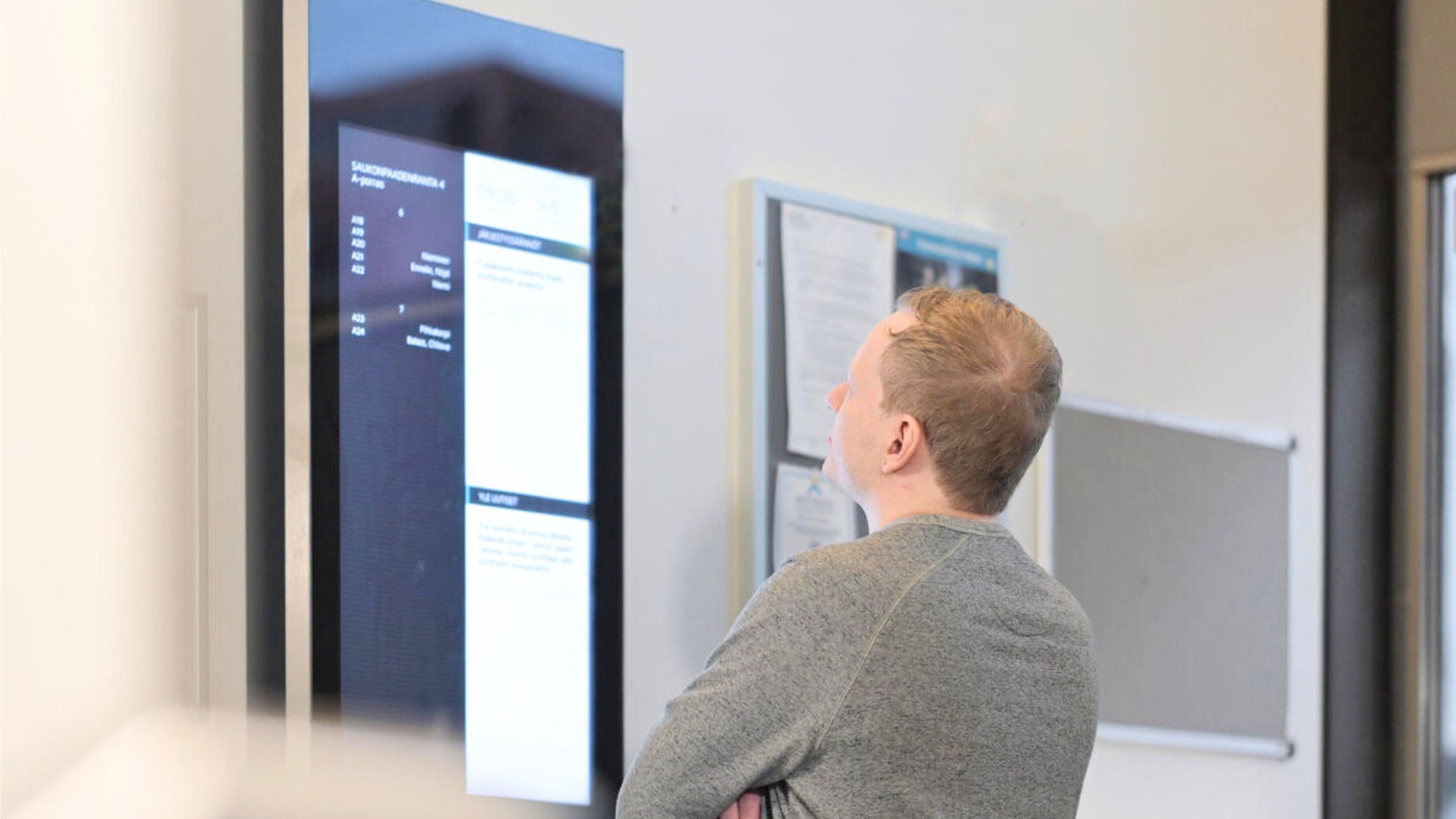 Henkilö seisoo rappukäytävässä lukemassa digitaalista ilmoitustaulua